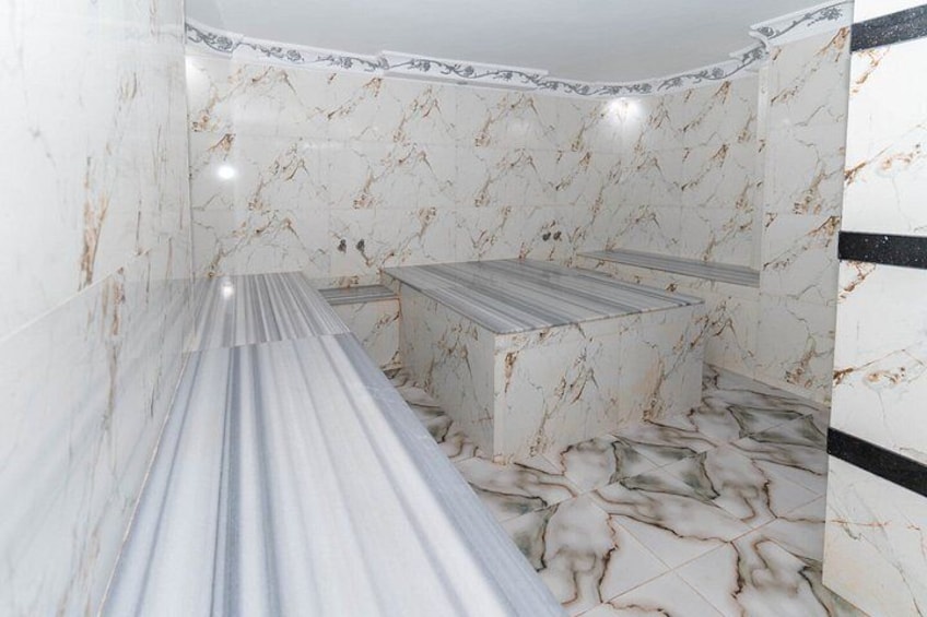 Un bagno con pareti e pavimenti in marmo, un lungo piano di lavoro e una fascia nera sulla parete. 5