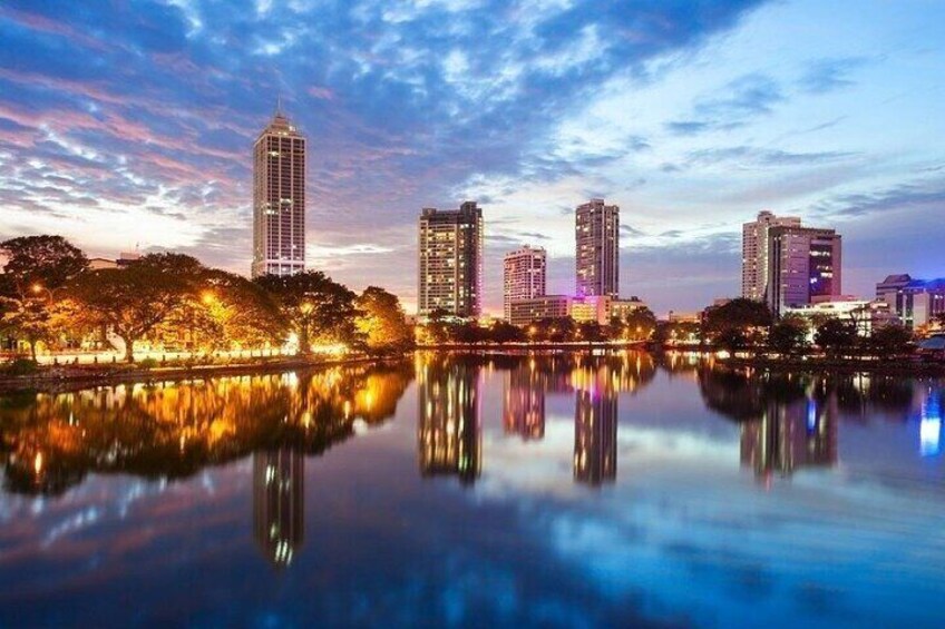 A city skyline at dusk with buildings reflected in a calm body of water. 1