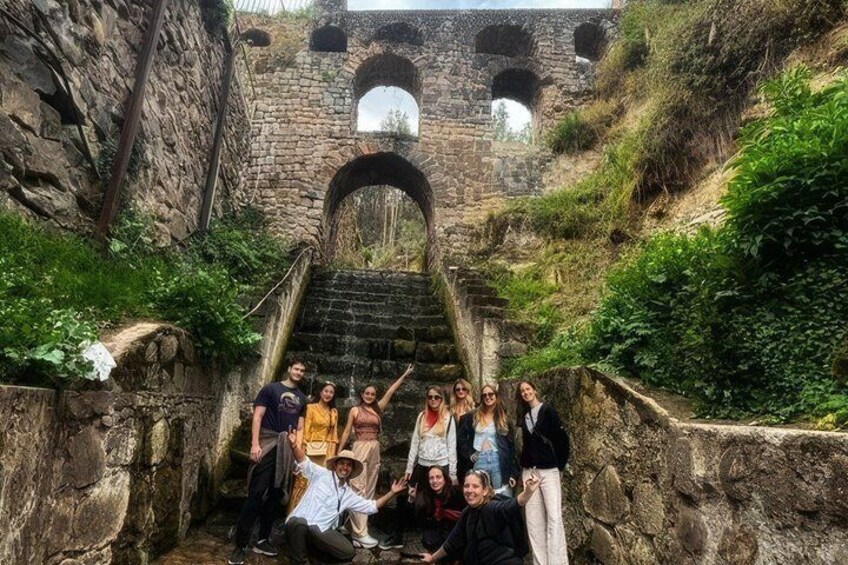 A group of people standing in front of a stone staircase leading to an arched bridge. 1