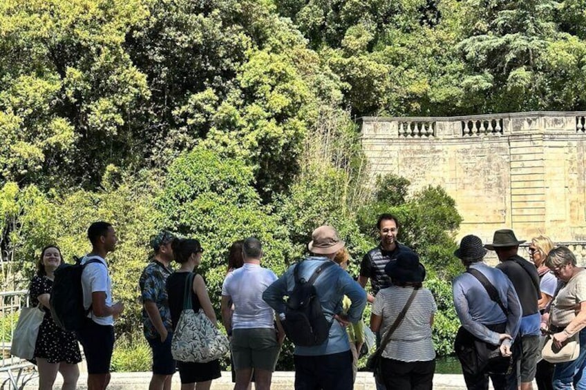 A group of people standing in a line, facing a stone wall with carvings, surrounded by trees. 1