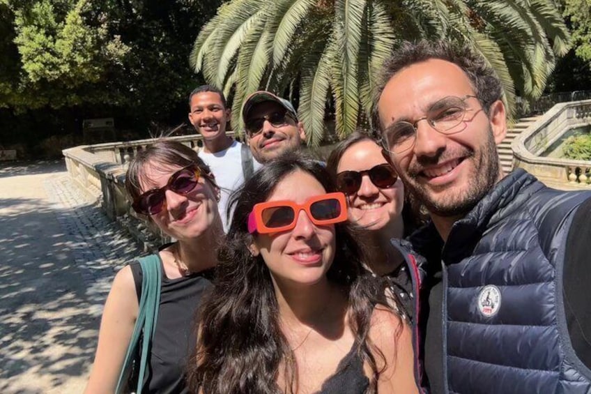 A group of people taking a selfie in a park with palm trees and a fountain in the background. 2