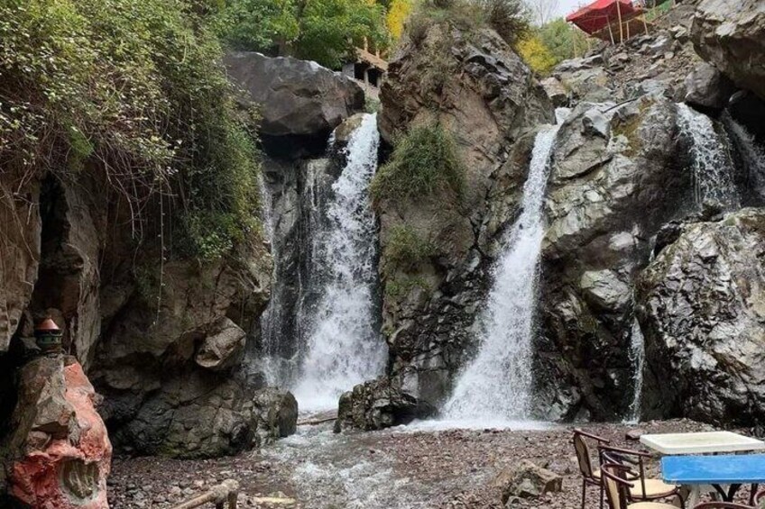 Una cascada que se precipita sobre terreno rocoso, con una mesa y sillas cerca. 5