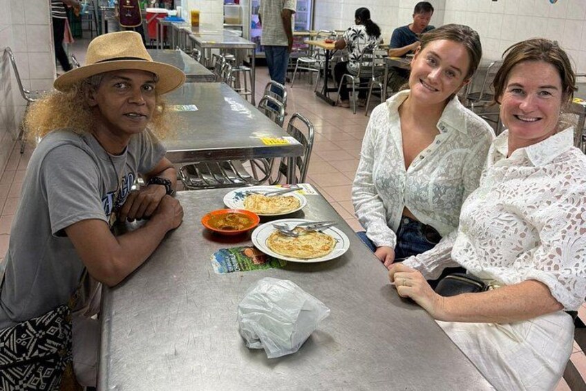 Tre personer sidder ved et cafeteriebord med mad og en servietkasse. 1