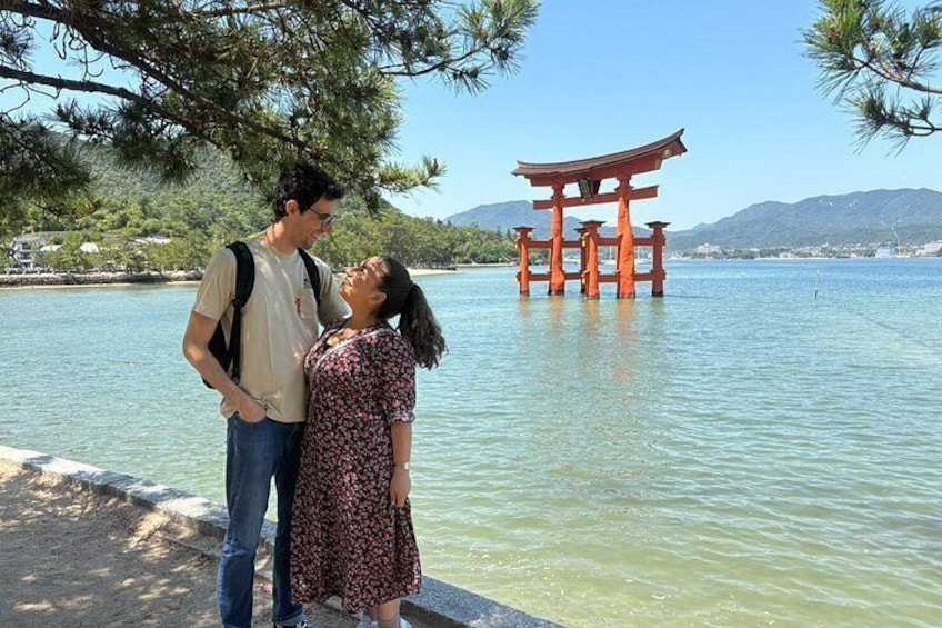 Una pareja de pie junto a un cuerpo de agua, con un torii japonés tradicional al fondo. 1