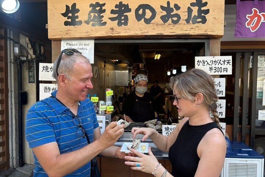 Un puesto de comida callejera con un letrero en japonés, un cliente interactuando con el vendedor y una persona de fondo. 2