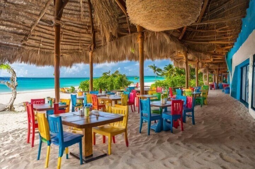 En restaurang vid stranden med färgglada stolar och bord, ett halmtak och utsikt över havet. 3