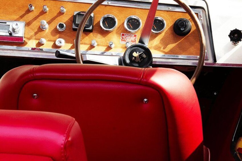 A vintage car interior with a red leather seat and a wooden dashboard with gauges. 2