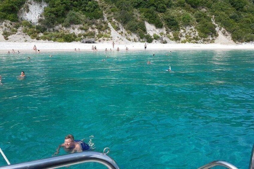 A clear turquoise sea with people swimming and sunbathing on a white sandy beach. 1