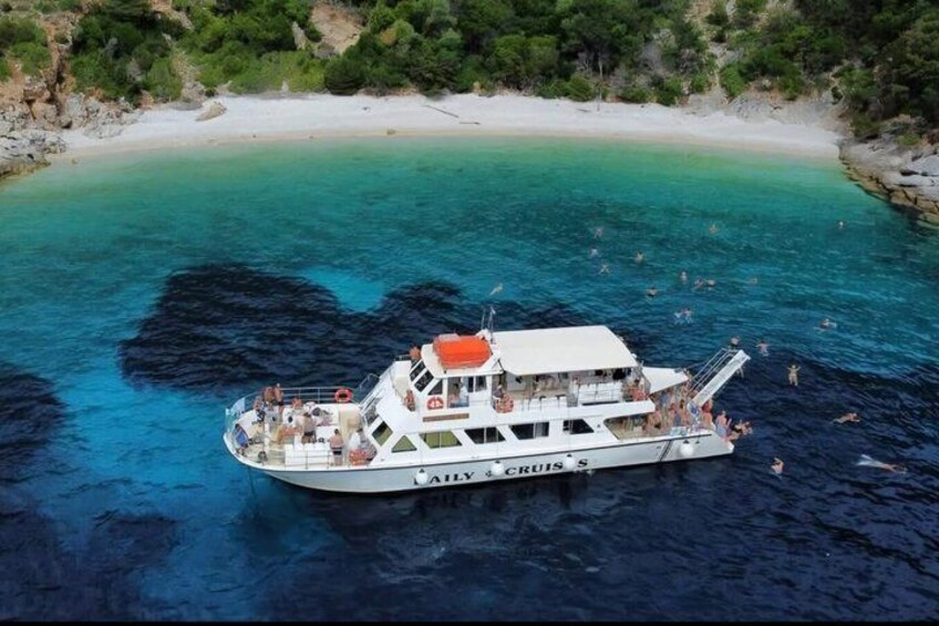 A boat named 'ALYX & FRITES' on clear turquoise waters with a beach and rocky coastline in the background. 3