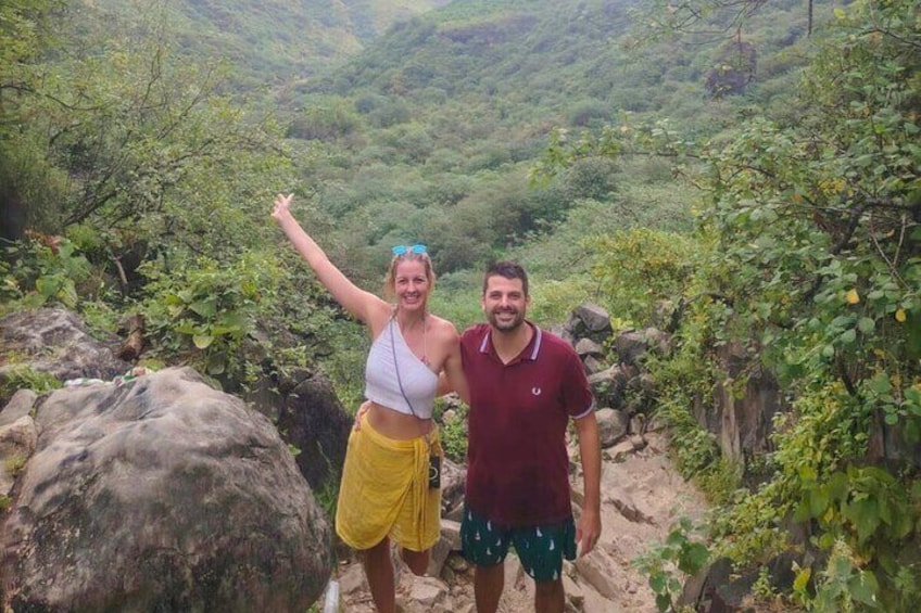 Two people standing on a rocky path surrounded by lush greenery. 3