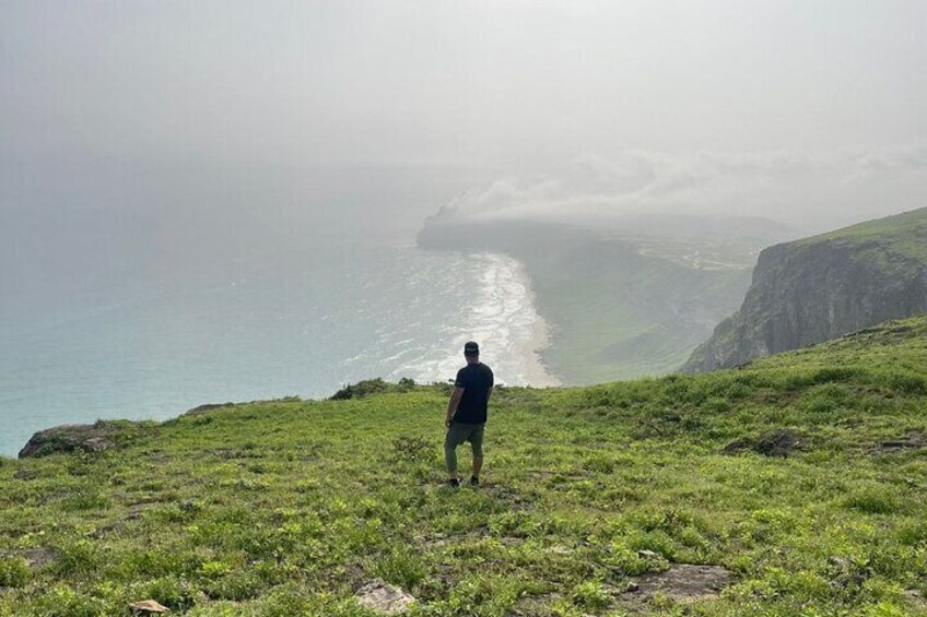 A person standing on a grassy hill overlooking a coastline with cliffs and a misty sea. 4