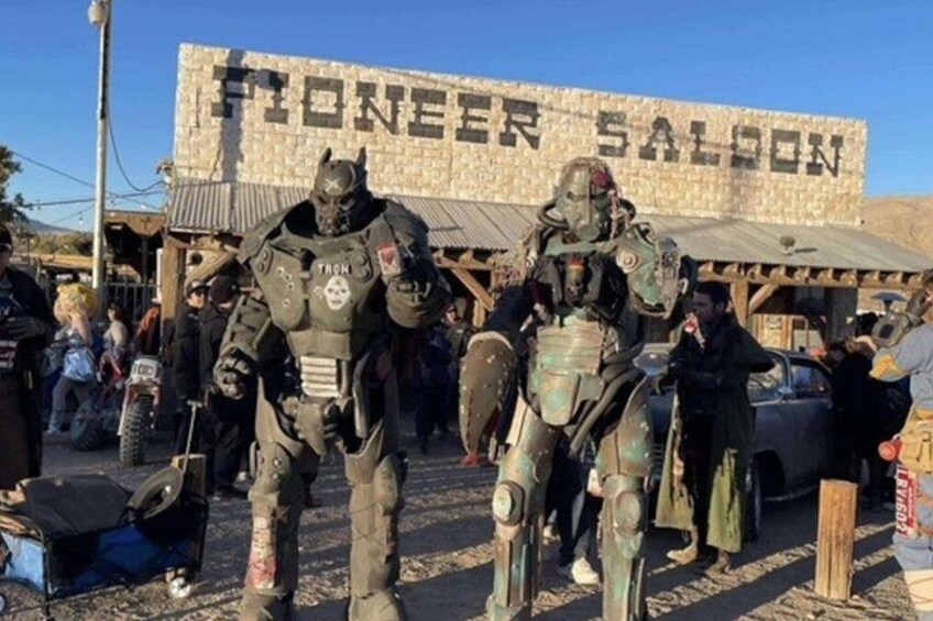 Dos personas con equipo táctico de pie frente a un edificio con un letrero que dice 'PIONEER SALOON'. 1