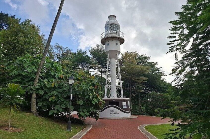 A white lighthouse with a red base, surrounded by lush greenery and a paved path leading to it. 5