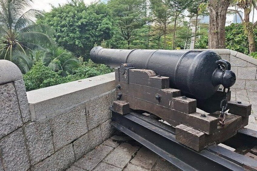 A large cannon mounted on a stone platform with a stone wall in the background. 3