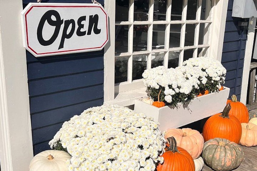 Una vetrina con il cartello 'Open', fiori bianchi e zucche. 3