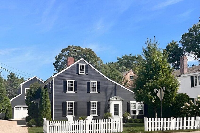 Une maison à deux étages, avec une façade de couleur gris foncé, des boiseries blanches et une clôture en bois peinte en blanc. 2