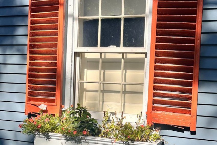 Et hus med lyseblå facade, et hvidt vindue og røde skodder. 3