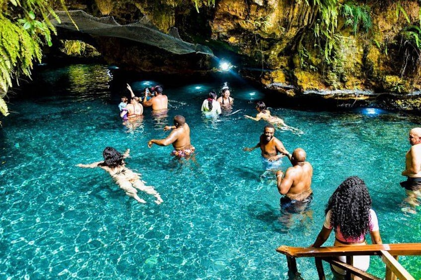 A group of people swimming in a clear blue pool surrounded by rocky cliffs. 4