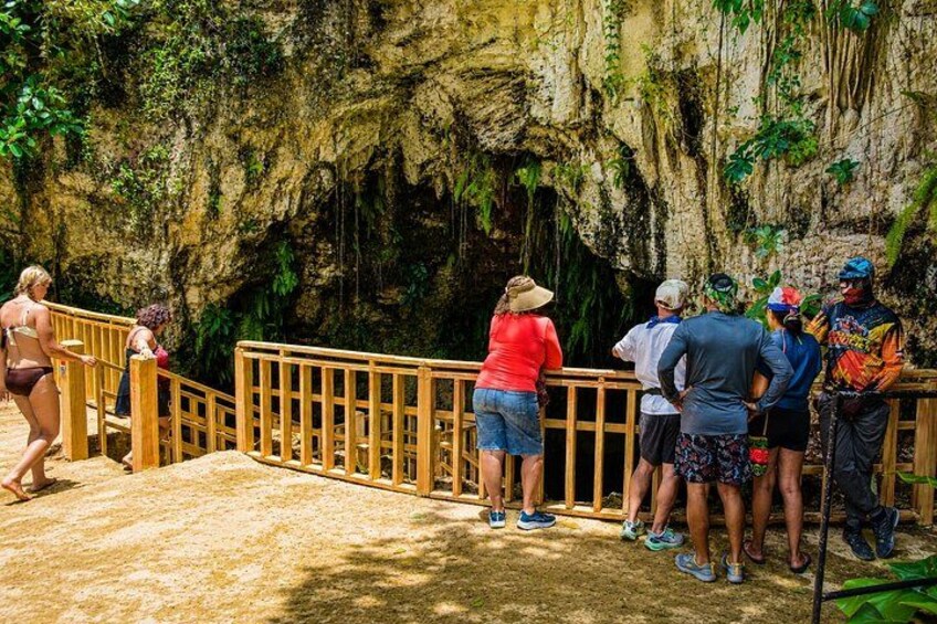 A group of people standing at a wooden railing overlooking a cave entrance. 5