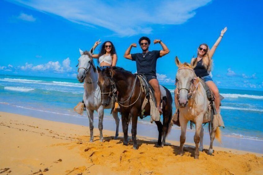 Three people riding horses on a beach with the ocean in the background. 2