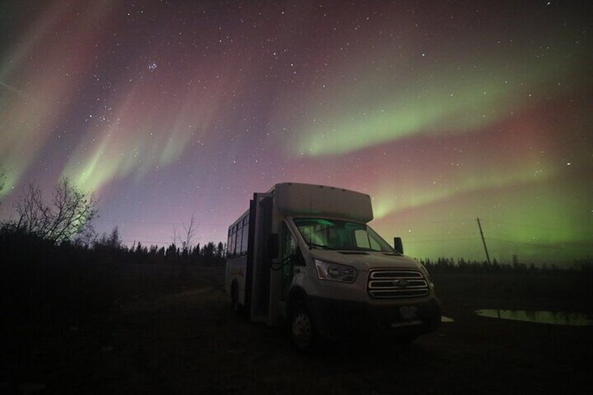 Una camioneta blanca estacionada en un campo bajo un cielo nocturno con la aurora boreal. 1