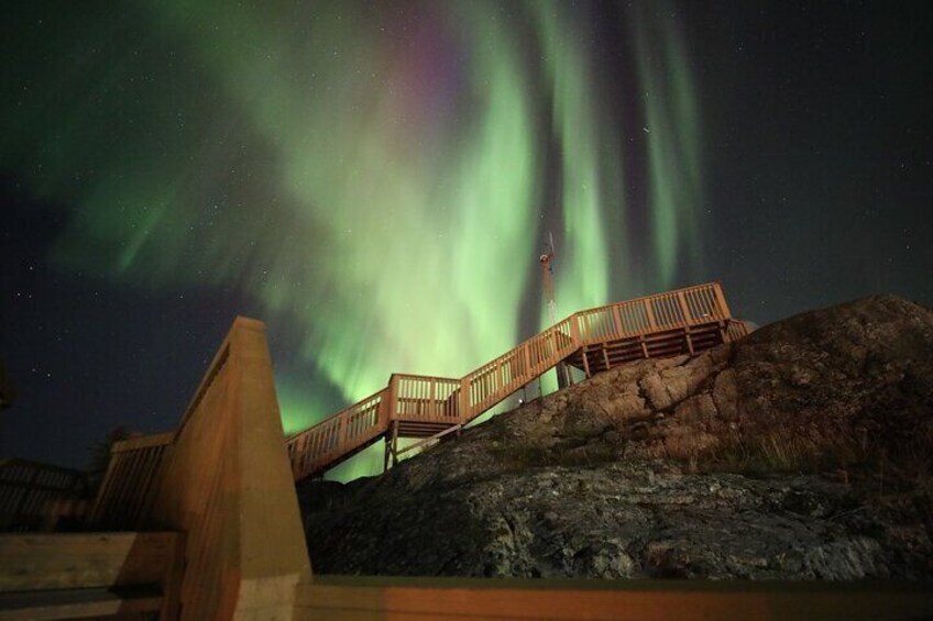 Una plataforma de madera con vistas a un paisaje rocoso, con la aurora boreal de fondo. 5
