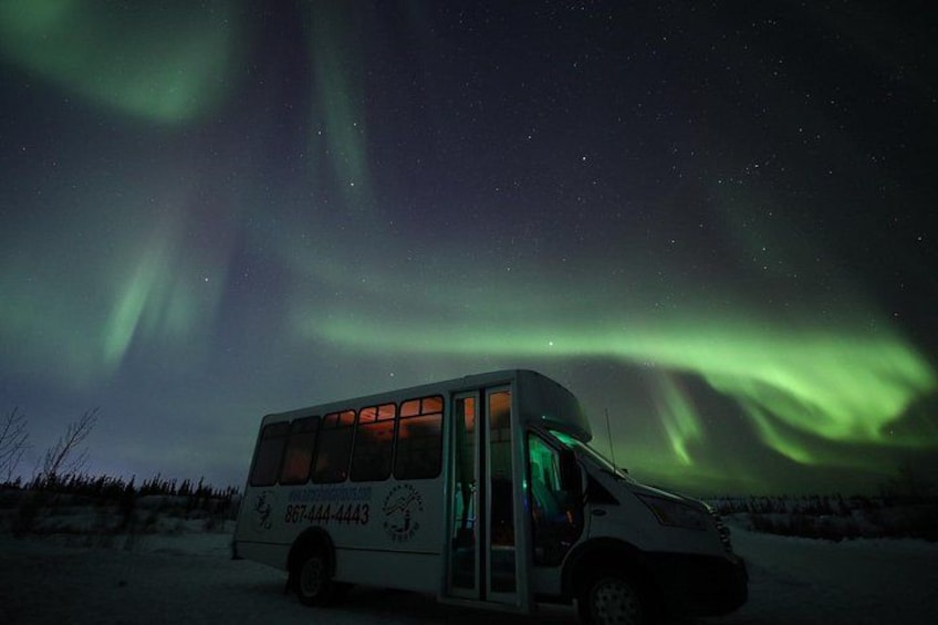 A bus parked in a snowy landscape under a night sky with the Northern Lights. 2