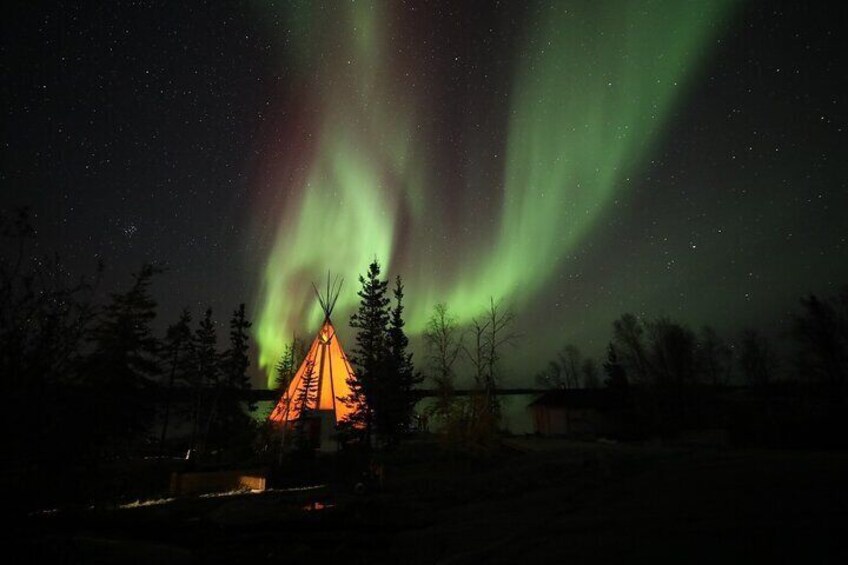 Un tipi iluminado contra un cielo nocturno con la aurora boreal. 4