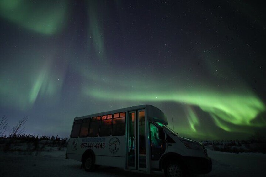 Un autobús estacionado en un paisaje nevado bajo un cielo nocturno con auroras boreales. 2