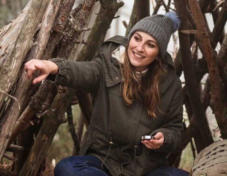 A person sitting among logs, wearing a jacket and holding a device. 5