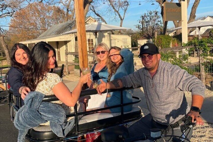 A group of people on a stationary bicycle, a wooden fence, and a building in the background. 5