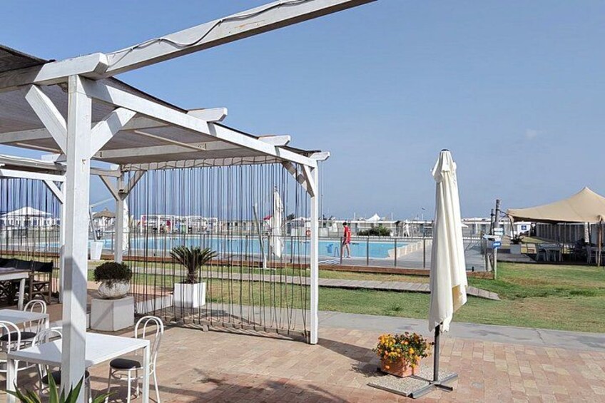 A covered outdoor seating area with a pool in the background. 2
