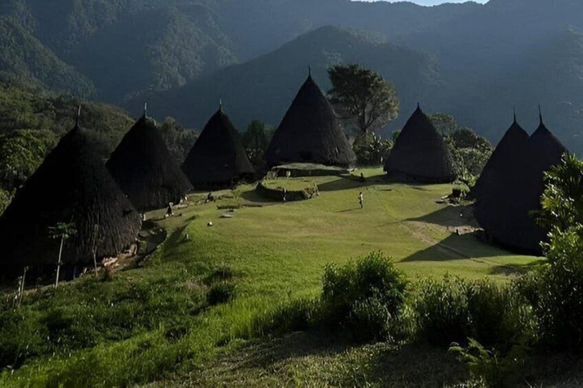 Thatched-roof huts in a grassy valley with mountains in the background. 4