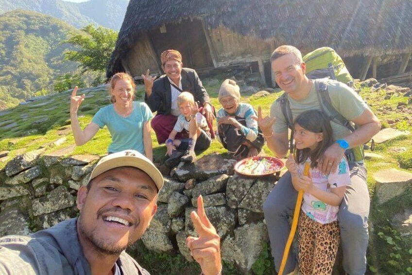 A group of people in a mountainous area with a thatched-roof structure in the background. 1