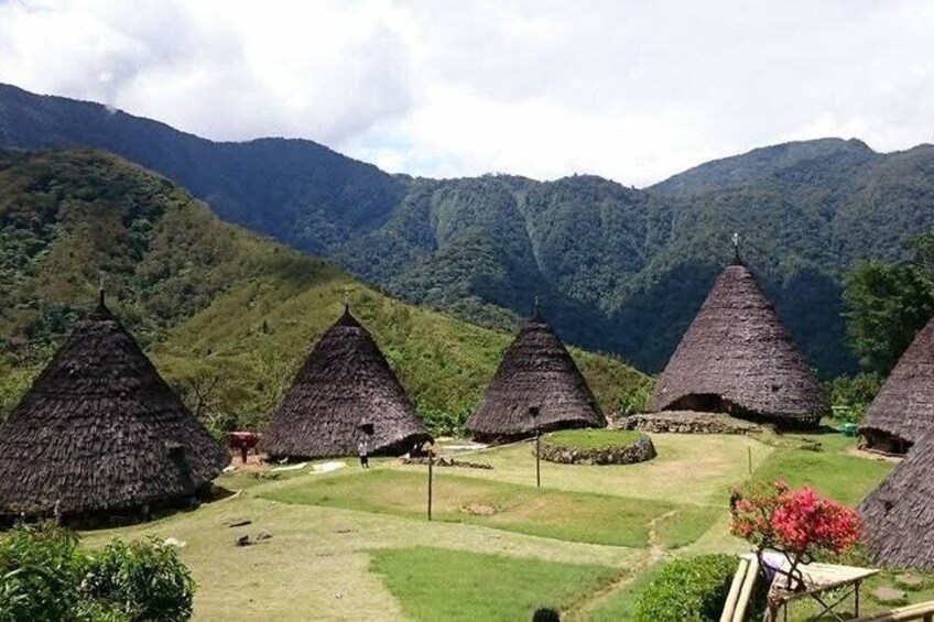 Thatched-roof huts in a valley with mountains in the background. 3