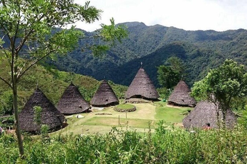 Thatched-roof huts in a lush valley with mountains in the background. 2