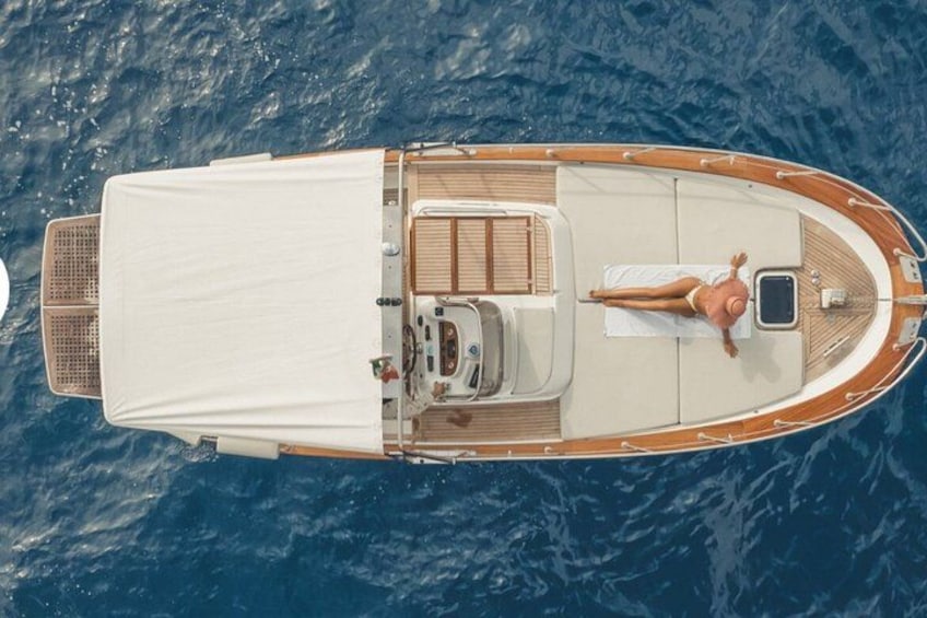 A boat with a white canopy, wooden deck, and a person lying on a lounge chair. 4