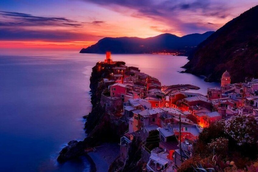 A coastal village at dusk with illuminated buildings and a mountain in the background. 3