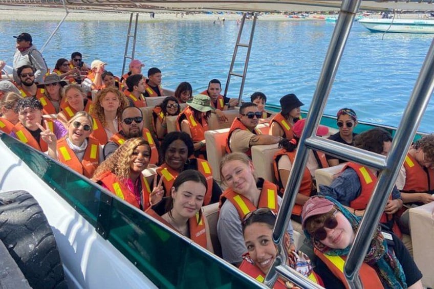 A group of people on a boat wearing life jackets, with water and a dock in the background. 1