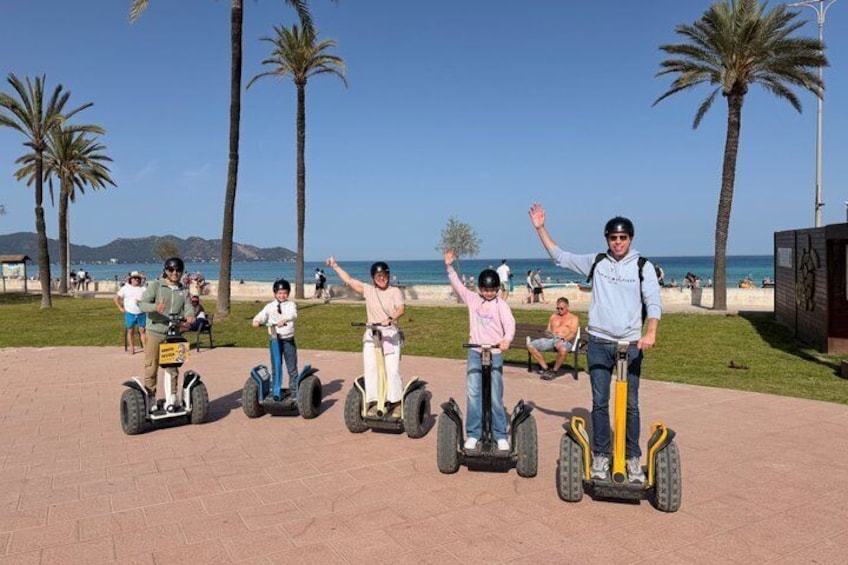 People on segways on a paved path with palm trees and a beach in the background. 1