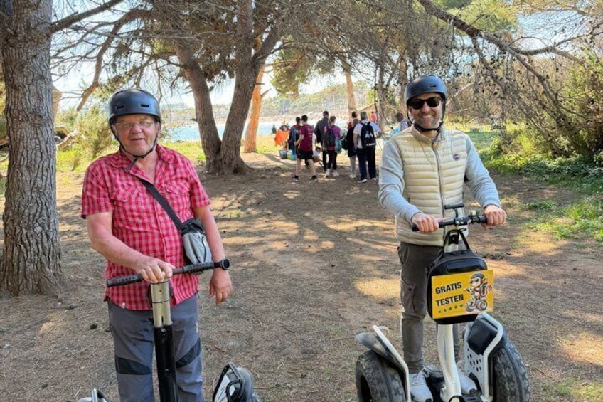 Two people on Segways in a wooded area with a sign that says 'GRATIS TESTEN' (free test). 3