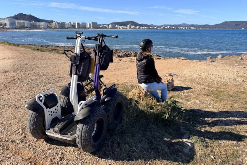 A person sitting on a rock by a body of water with a quad bike in the foreground. 2