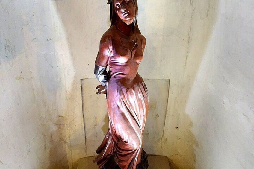 Une statue de bronze représentant une femme en robe, debout dans une pièce aux murs sobres. 2