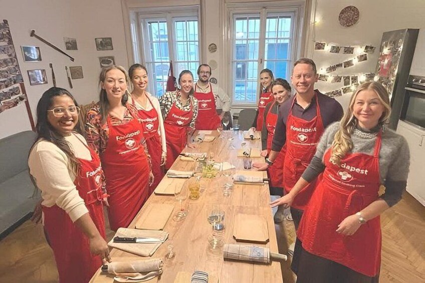 A group of people in aprons standing around a table with food items. 2