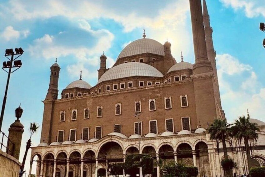 En stor moské med flere kupler og minareter, omgivet af palmer og en klar himmel. 1