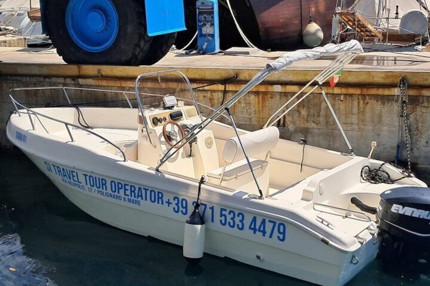 Ein kleines, weißes Boot liegt in einer Marina festgemacht. Es hat ein blaues Führerhaus, ein Steuer und eine Telefonnummer an der Seite. 2