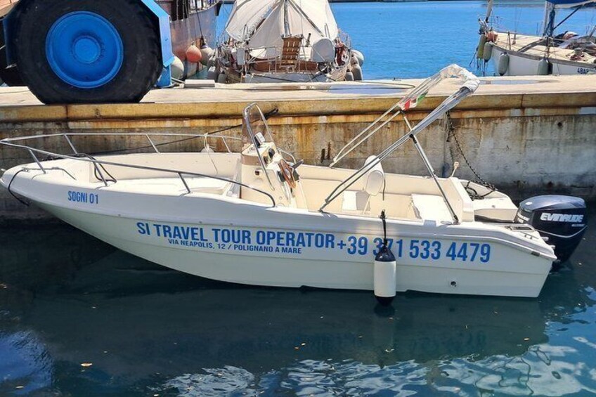 Ein weißes Boot liegt in einer Marina festgemacht, mit einer Telefonnummer und einem Namen, der darauf hindeutet, dass es sich um einen Reiseveranstalter handelt. 3
