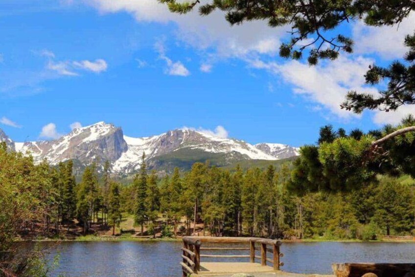 A lake with a wooden dock, surrounded by dense forest and snow-capped mountains in the background. 2