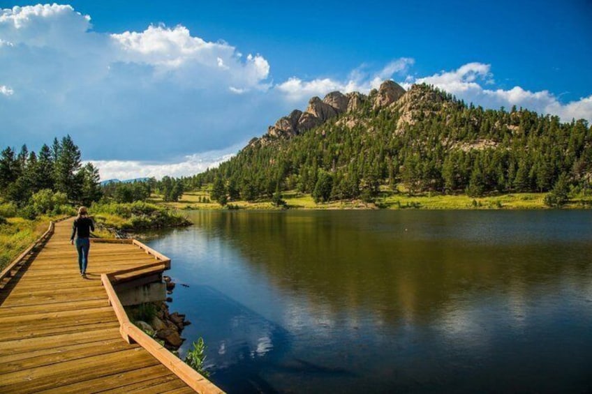 A wooden boardwalk by a calm lake with mountains in the background. 1