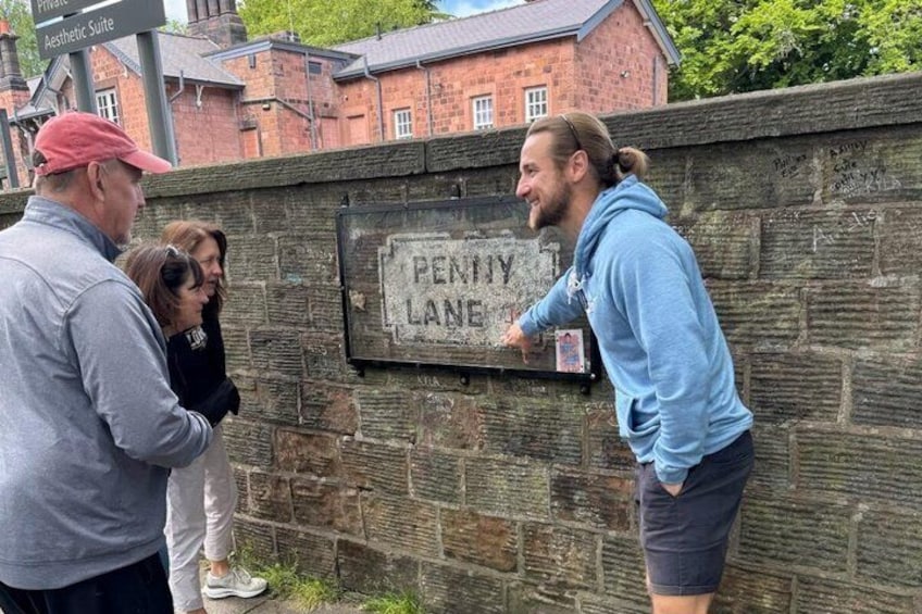 En gruppe mennesker står foran en stenvæg med et skilt, der siger 'Penny Lane'. 1